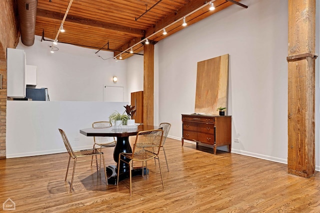 dining room featuring a towering ceiling, wooden ceiling, wood finished floors, rail lighting, and beam ceiling