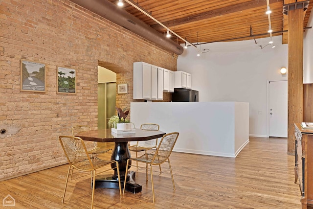 dining area with a towering ceiling, brick wall, light wood-type flooring, and track lighting