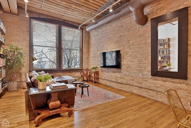 interior space with brick wall, wood finished floors, a towering ceiling, and track lighting