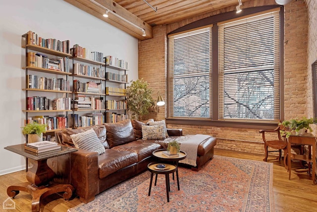 living area with wood ceiling, rail lighting, brick wall, and wood finished floors