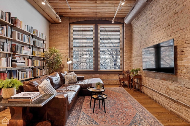 sitting room with rail lighting, a towering ceiling, brick wall, and wood finished floors