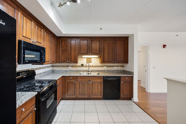 kitchen featuring light stone counters, a sink, brown cabinets, black appliances, and tasteful backsplash