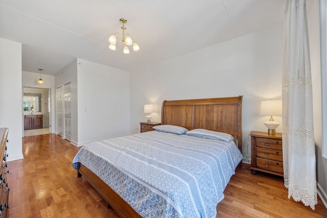 bedroom featuring baseboards, a notable chandelier, ensuite bath, and light wood finished floors