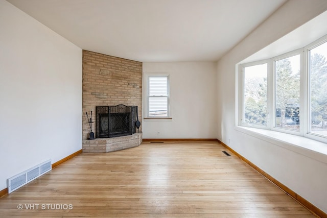 unfurnished living room featuring a healthy amount of sunlight, visible vents, a fireplace, and light wood-style flooring