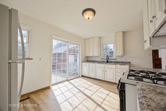 kitchen with gas range oven, light wood-type flooring, a sink, and freestanding refrigerator