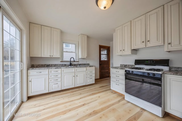 kitchen with light wood-style flooring, dark stone countertops, a sink, and gas range