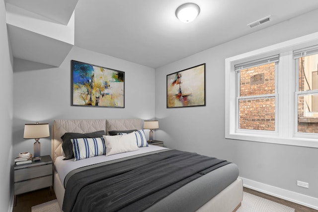 bedroom with multiple windows, wood finished floors, visible vents, and baseboards