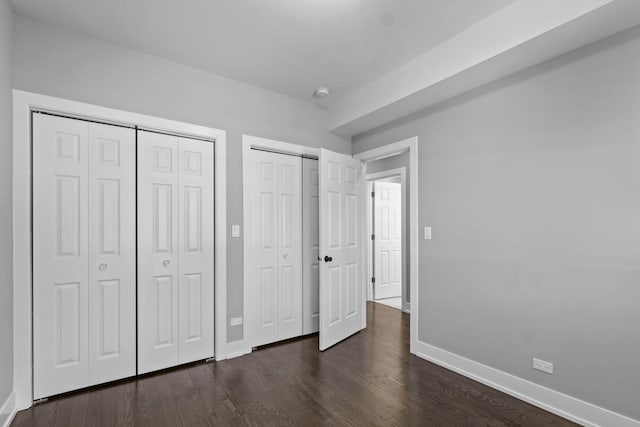 unfurnished bedroom featuring baseboards, dark wood-type flooring, and multiple closets