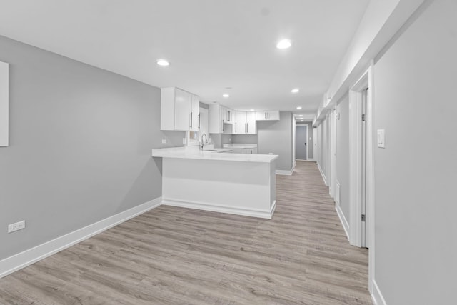 kitchen with baseboards, a peninsula, light countertops, white cabinetry, and a sink