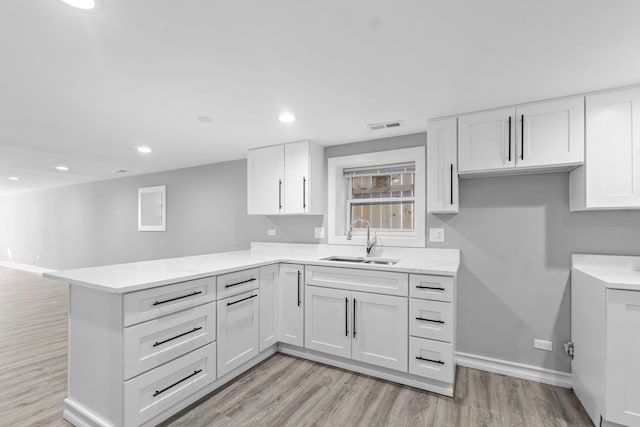 kitchen featuring a peninsula, a sink, visible vents, and white cabinets