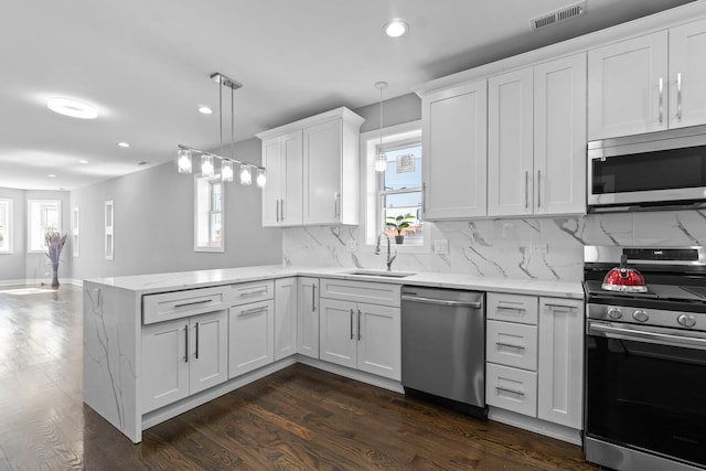 kitchen with decorative light fixtures, appliances with stainless steel finishes, white cabinetry, a sink, and a peninsula