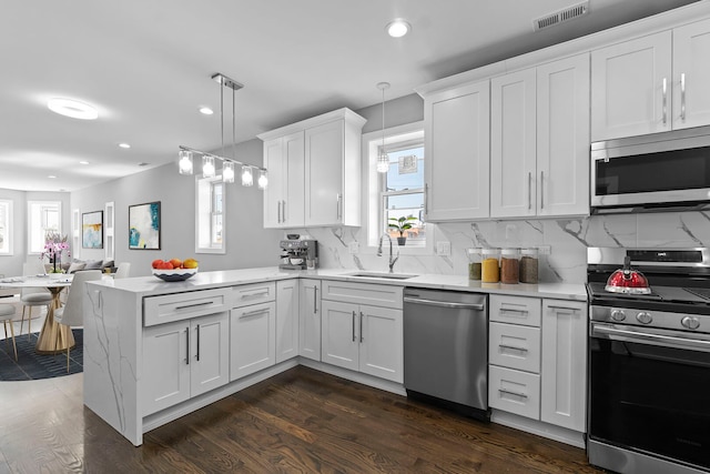 kitchen with appliances with stainless steel finishes, light countertops, hanging light fixtures, and a sink