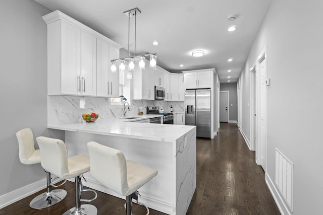 kitchen with stainless steel appliances, decorative light fixtures, a peninsula, and white cabinetry