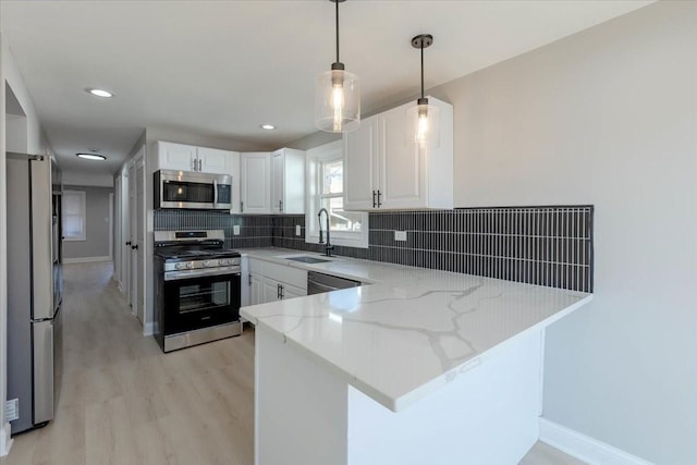 kitchen featuring stainless steel appliances, a peninsula, a sink, white cabinetry, and hanging light fixtures