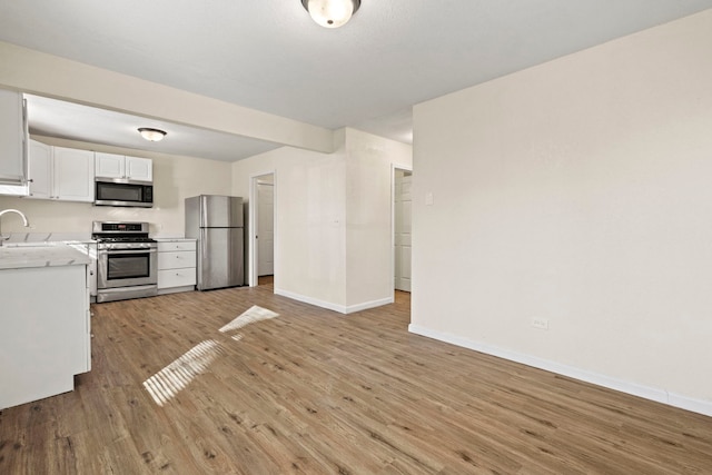 kitchen featuring light countertops, appliances with stainless steel finishes, white cabinets, a sink, and light wood-type flooring