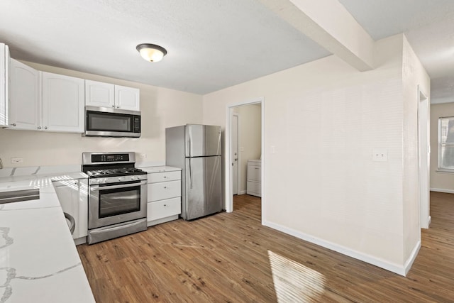 kitchen featuring light wood finished floors, baseboards, stainless steel appliances, light countertops, and white cabinetry