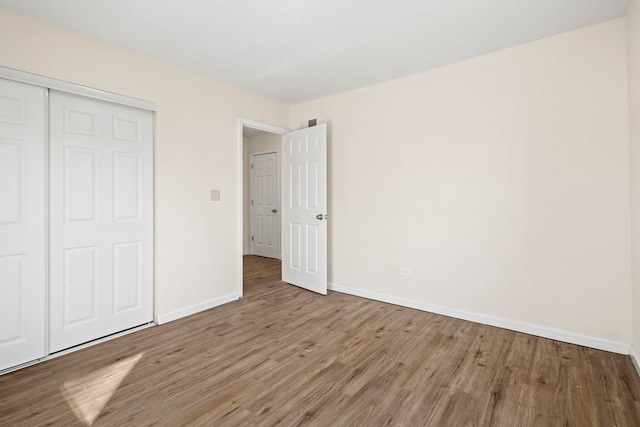 unfurnished bedroom with a closet, wood finished floors, visible vents, and baseboards