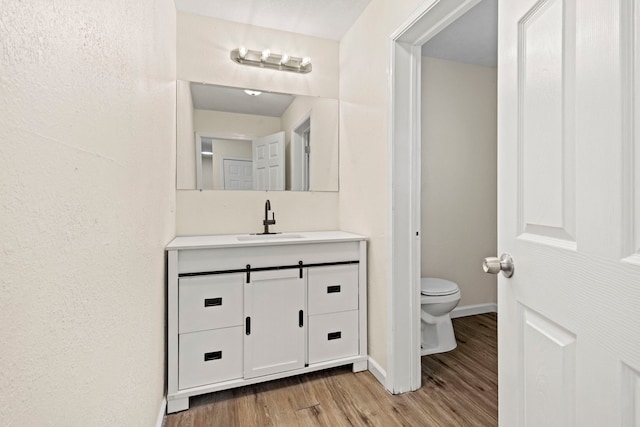 bathroom featuring baseboards, vanity, toilet, and wood finished floors