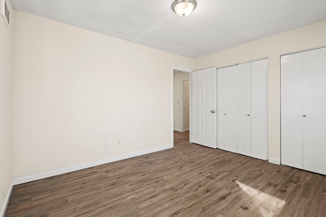 unfurnished bedroom featuring baseboards, wood finished floors, visible vents, and multiple closets