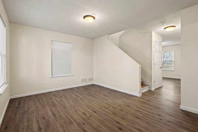 unfurnished room with dark wood finished floors, a textured ceiling, baseboards, and stairs