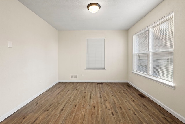 unfurnished room with baseboards, visible vents, and wood finished floors