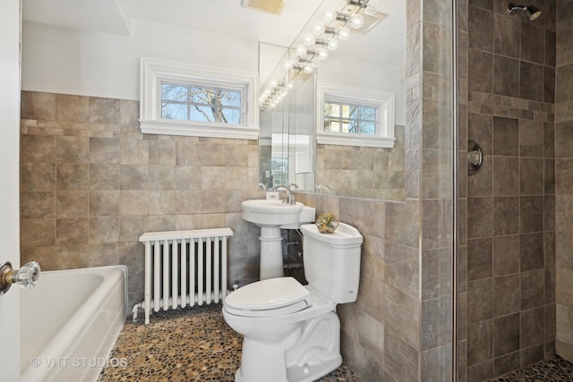 bathroom with tiled shower, toilet, radiator heating unit, a washtub, and tile walls