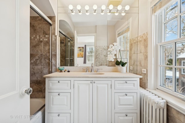 bathroom featuring a healthy amount of sunlight, tile walls, vanity, and radiator