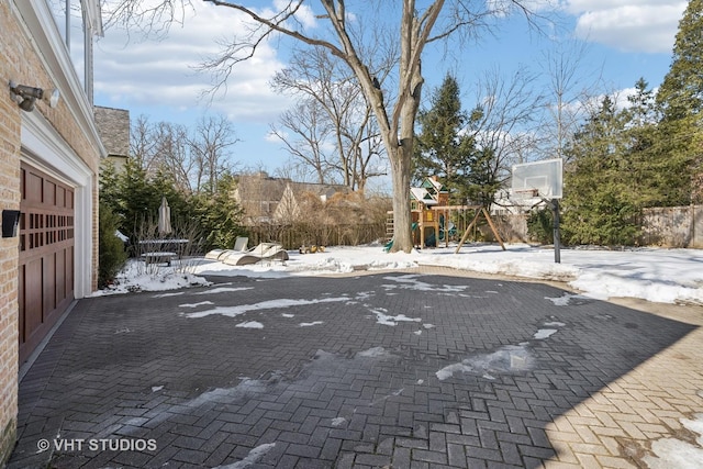 snow covered patio featuring a garage, fence, and a playground