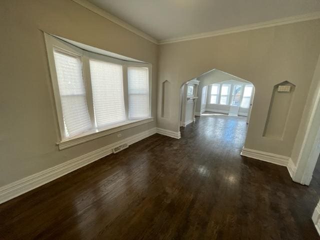 interior space with arched walkways, dark wood-style flooring, visible vents, baseboards, and ornamental molding