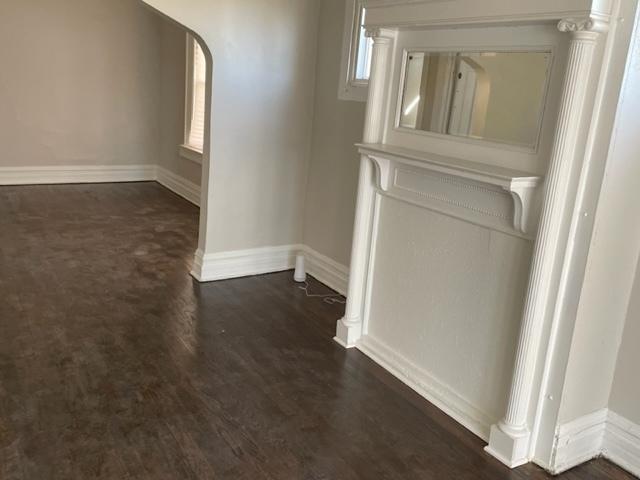 corridor featuring arched walkways, dark wood-style flooring, and baseboards