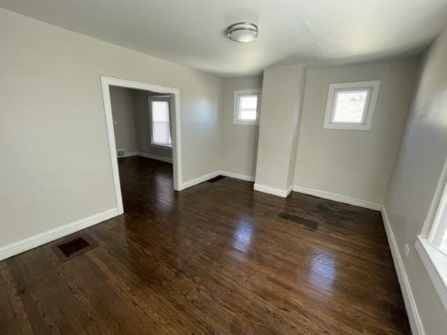 spare room featuring dark wood-style flooring, visible vents, and baseboards