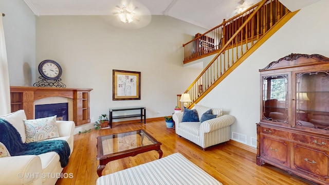 living area with ornamental molding, wood finished floors, a glass covered fireplace, and baseboards