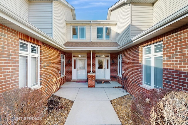 property entrance with a shingled roof and brick siding