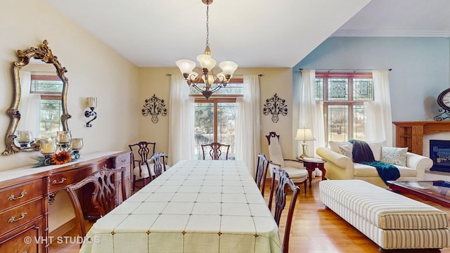 dining space with lofted ceiling, a glass covered fireplace, wood finished floors, and a notable chandelier