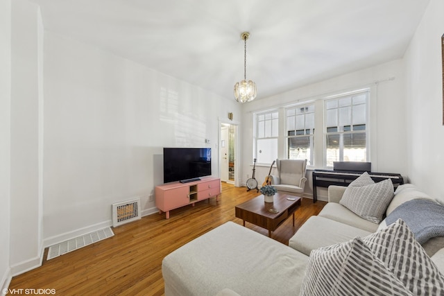 living area with baseboards, wood finished floors, visible vents, and an inviting chandelier