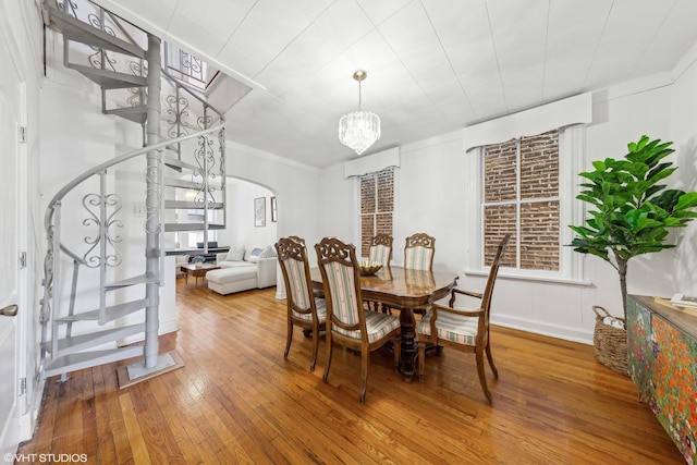 dining area with arched walkways, wood finished floors, stairs, and a notable chandelier