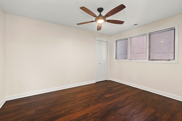 unfurnished room with dark wood-style floors, visible vents, baseboards, and a ceiling fan