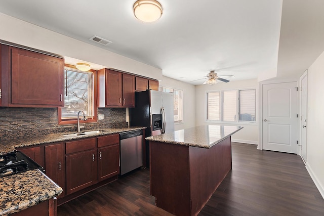 kitchen featuring a center island, stainless steel appliances, visible vents, a sink, and dark stone counters