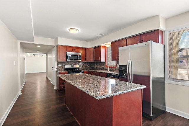 kitchen featuring tasteful backsplash, dark stone counters, a kitchen island, appliances with stainless steel finishes, and dark brown cabinets