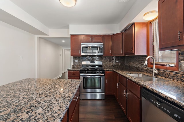 kitchen featuring dark wood finished floors, dark stone counters, a sink, stainless steel appliances, and backsplash