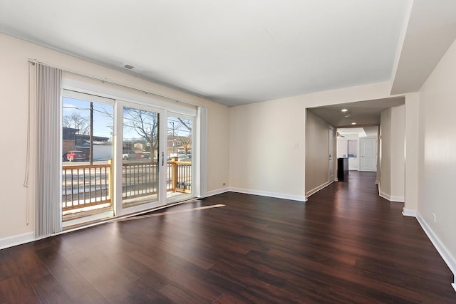 empty room featuring visible vents, baseboards, and dark wood finished floors