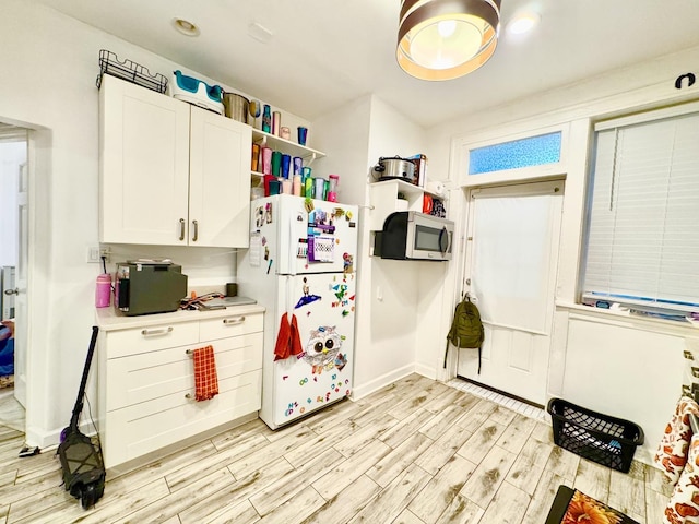 kitchen with white cabinets, light countertops, light wood-type flooring, freestanding refrigerator, and stainless steel microwave