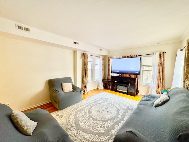 living room with light wood-type flooring, visible vents, and baseboards