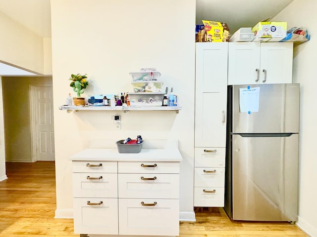 kitchen featuring baseboards, white cabinets, light countertops, light wood-type flooring, and freestanding refrigerator