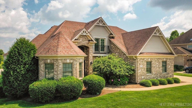 view of front of home featuring brick siding, a front yard, a balcony, and a shingled roof