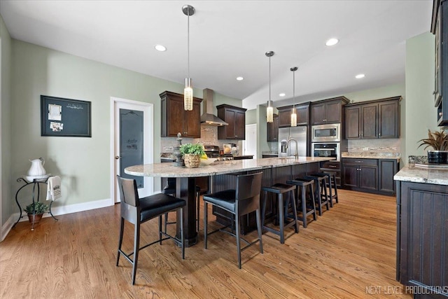 kitchen featuring stainless steel appliances, dark brown cabinets, wall chimney exhaust hood, and a large island