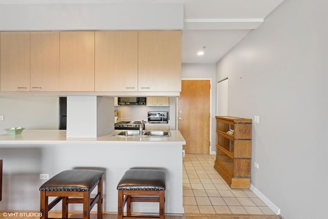 kitchen featuring a breakfast bar, light countertops, light tile patterned flooring, a sink, and black microwave