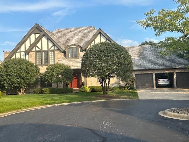 tudor home with driveway, a garage, a front yard, and stucco siding