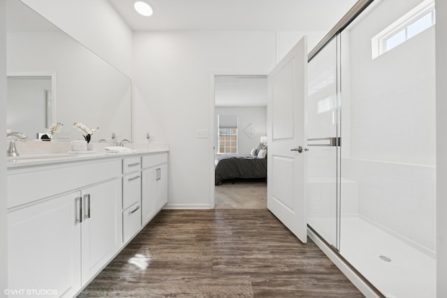 ensuite bathroom with a tile shower, wood finished floors, a sink, and connected bathroom