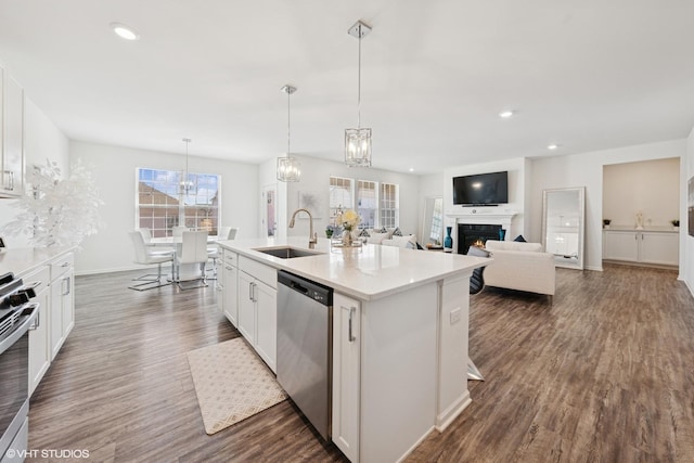 kitchen featuring dark wood finished floors, a lit fireplace, a kitchen island with sink, stainless steel appliances, and a sink